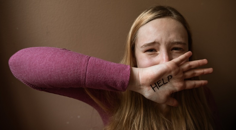 Frightened teen girl with hand over her face saying, "Help."