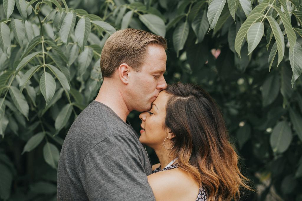 Husband hugs his wife as he kisses her forehead.