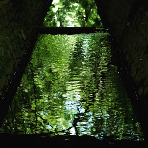 green and blue water in some kind of reservoir, surrounded by dark sides. the water is lit up by the reflection of trees. 