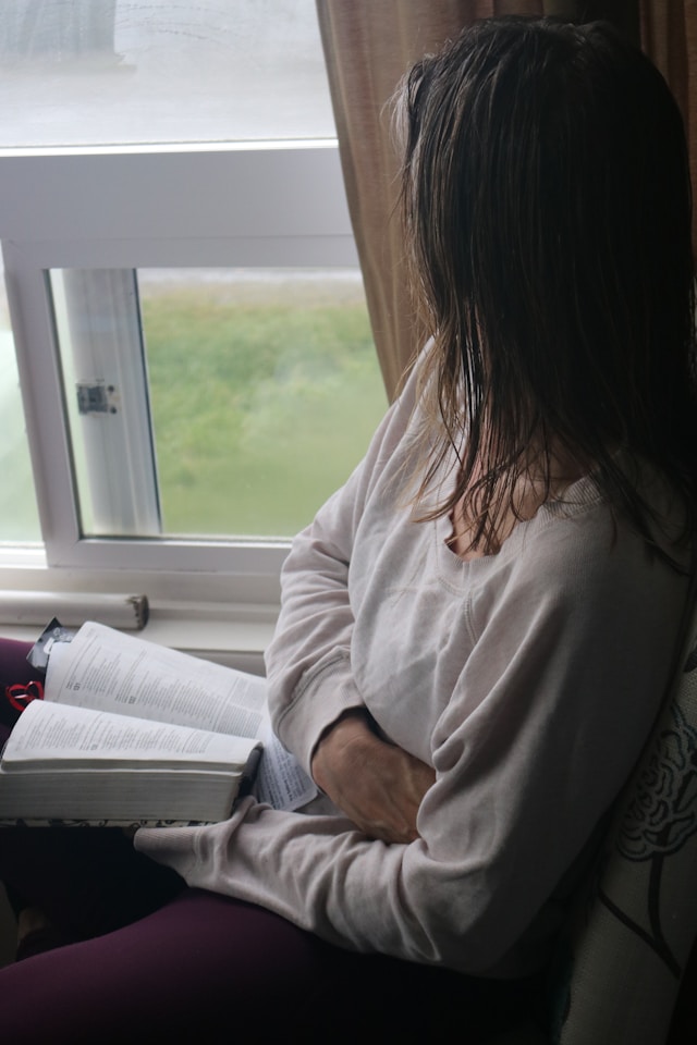 Person writing in journal by window reflecting on God's provision and documenting faith journey