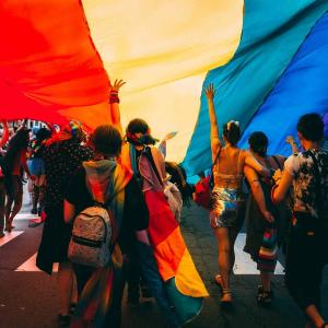 Image of pride celebration under a large rainbow flag