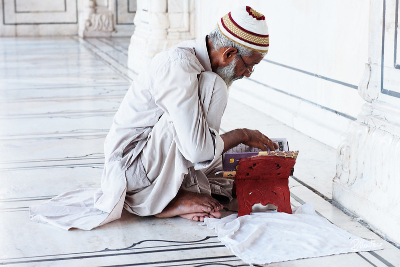 A Muslim man kneels in prayer with the Qur'an