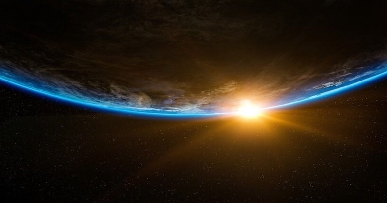 A view of earth from space, hanging in darkness with the sun kissing its horizon