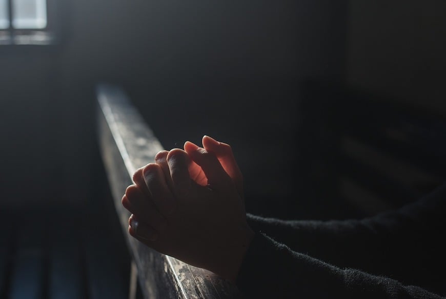 hands clasped in prayer in a church pew