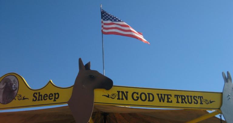 "In God we trust" sign with American flag in the background