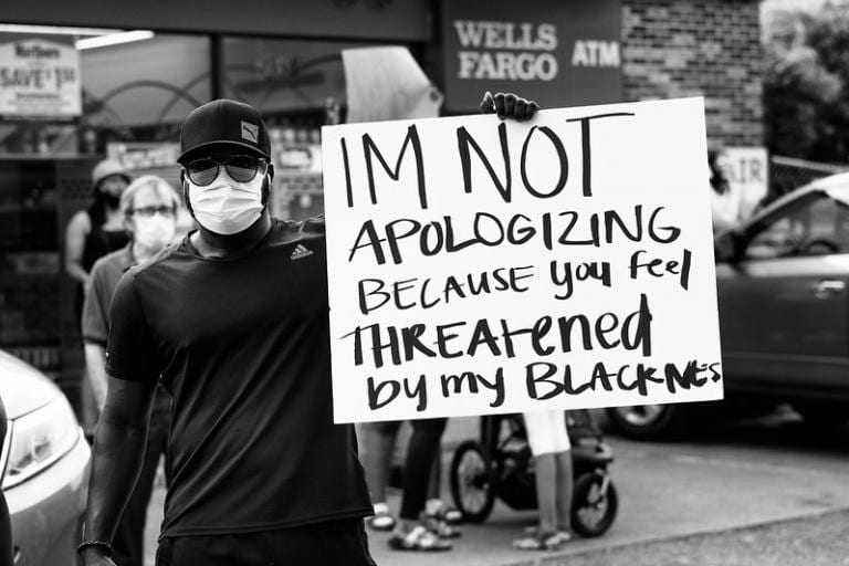 Protestor holding sign: "I'm not apologizing because you feel threatened by my blackness"