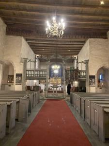 a picture of the interior of a medieval church, Trondenes Kirke, with lime-washed white walls, wooden pews, a wooden ceiling, and a decorated wooden rood screen