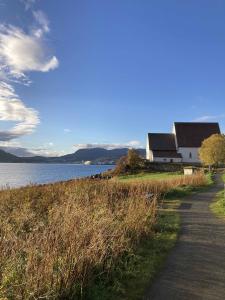 Trondenes Kirke. A white stone church against blue water and a field