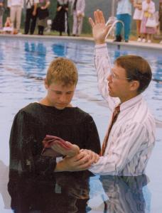 man baptizing teenage boy in swimming pool