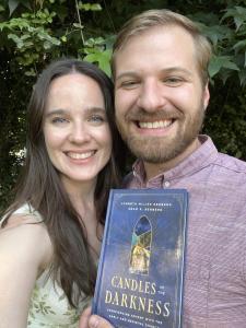 Two very happy authors holding a book with a blue and gold cover, titled "Candles in the Darkness."