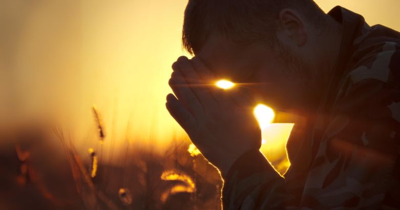 A man fervently praying to God at sunset