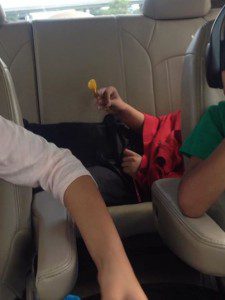 Lil D lying down in the back seat, arms drawn in, hood up, spinning his beads, at the end of a very long road trip.