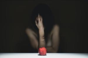 Indistinct woman with hand over face and red apple in foreground