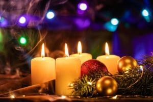 Four lit candles and an ornament in the foreground with a Christmas tree in the background