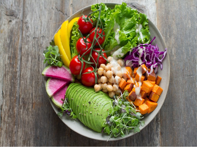 Roasted vegetable bowl with roasted sweet potatoes, chickpeas, avocado, cabbage, salad greens, and salad dressing,.