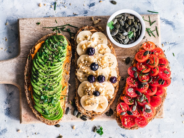 Avocado toast, fruit toast, and tomato toast, arranged on a cutting board.