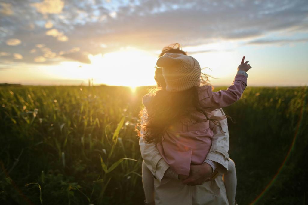 mother holding daughter in field with sunset behind them