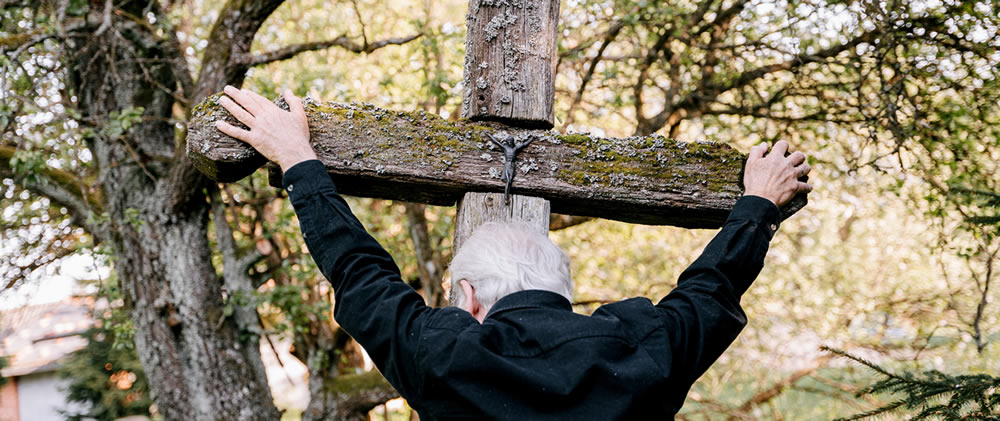 An older man holding a very old wooden cross - contemplating the crucifixion