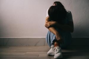 A person sits next to a wall with head between their arms. 