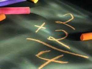 2+2=4 written on chalkboard with multi-colored pieces of chalk lying about