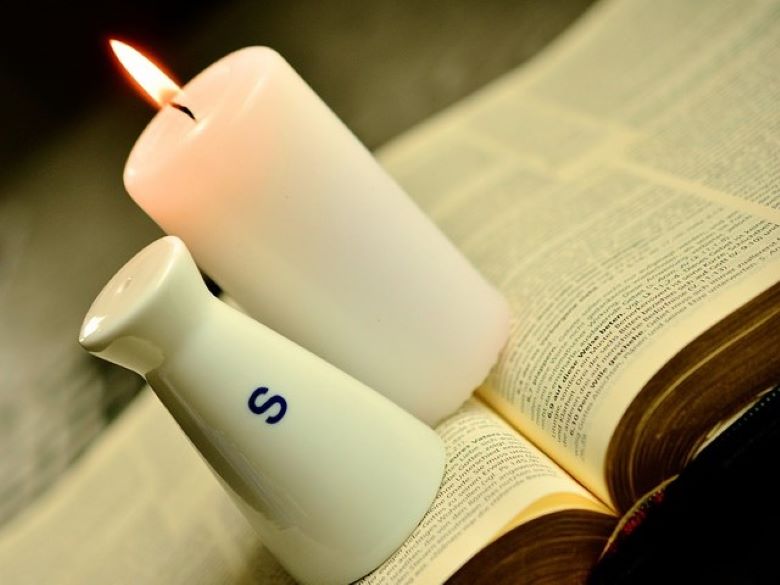 Tilted image of salt shaker and lit candle on an open Bible