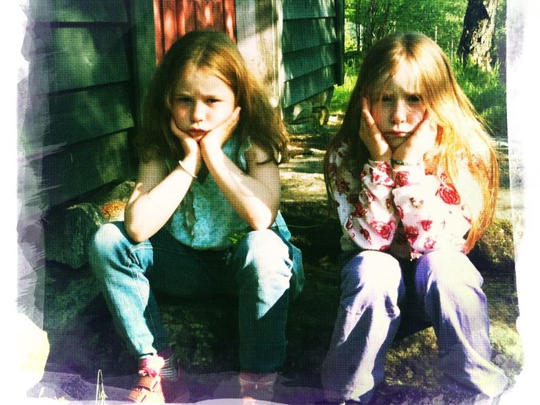 Two young girls sitting on the porch steps looking disgusted with each other