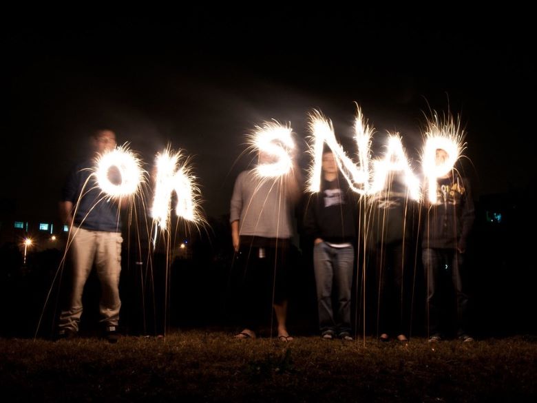 "Oh Snap" outlined in sparklers against a dark background with the people who lit the sparklers standing behind them
