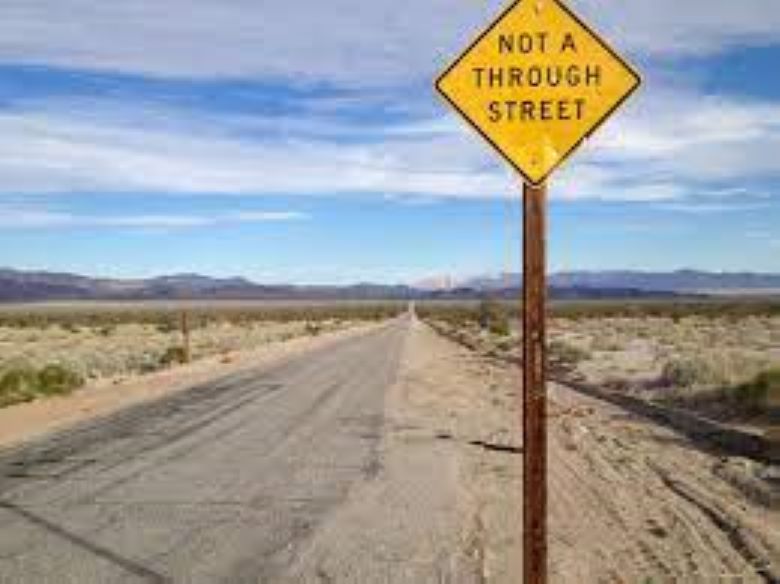 Road leading into the desert toward the horizon with a road sign reading "Not a Through Street"