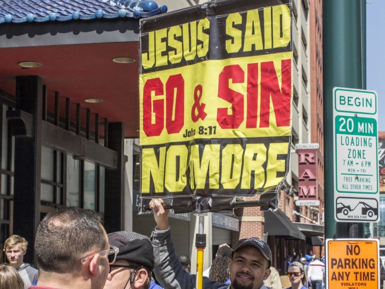 Man in crowd with sign quoting John 8:11