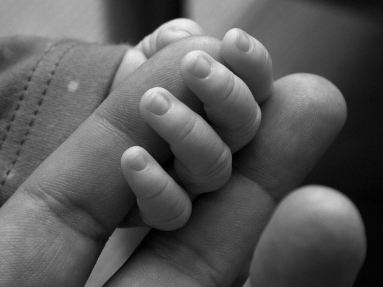 black and white close-up of a baby's hand holding an adult finger