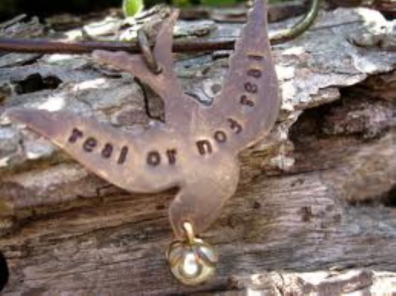 Mockingjay pendant with "Real or not real" printed across the wings, set on a log in the woods