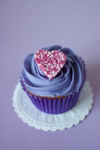 A single cupcake with blue frosting and a heart sprinkles decoration on top.