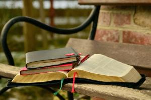 Two notebooks on top of an open bible sitting on a bench
