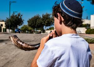 A Jewish boy stands on a sunny street blowing a shofar (ram's horn).