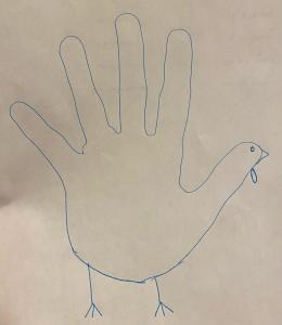 Outline of a hand traced on white paper, with the addition of legs, beak, and waddle to turn it into a turkey.