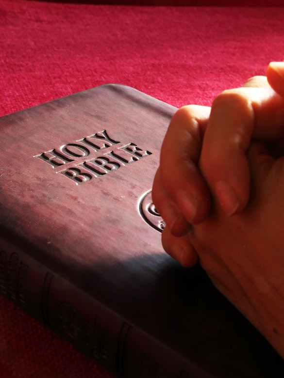 two hands clasped in prayer upon a Holy Bible