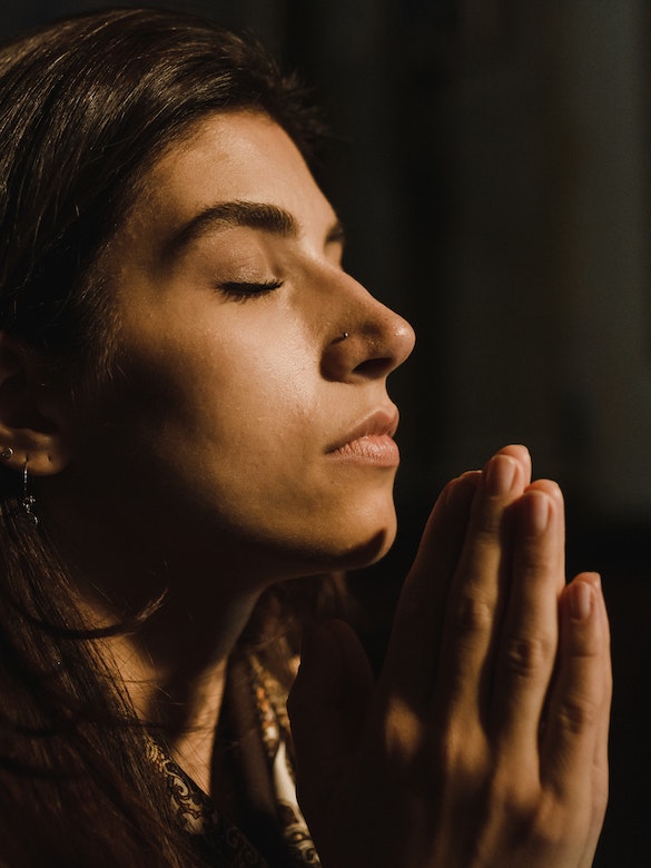 A young woman prays earnestly with hands clasped and eyes shut