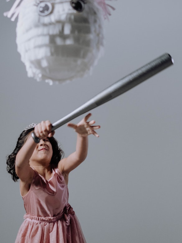 A young girl in a pink dress swings a baseball bat at a candy stuffed pinata