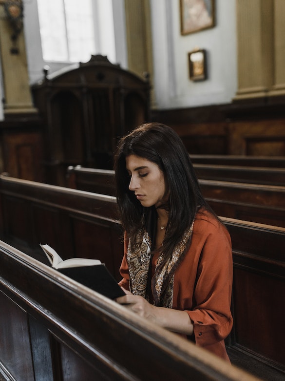 a lone woman studies the scriptures in a pew at church