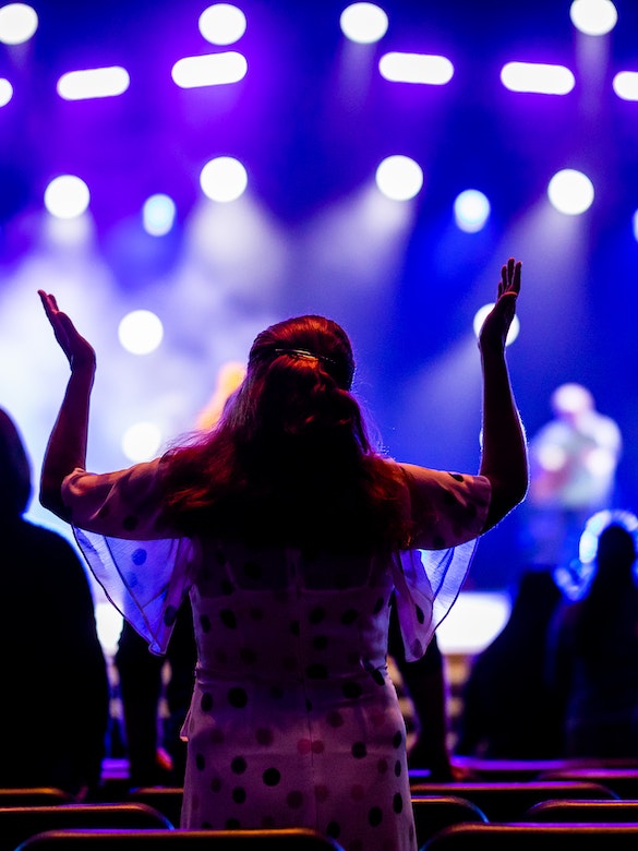 A woman raises her hands during worship and surrenders to the Lord