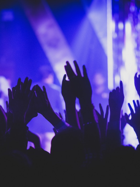 A group of people raise their hands as they worship and surrender to the Lord