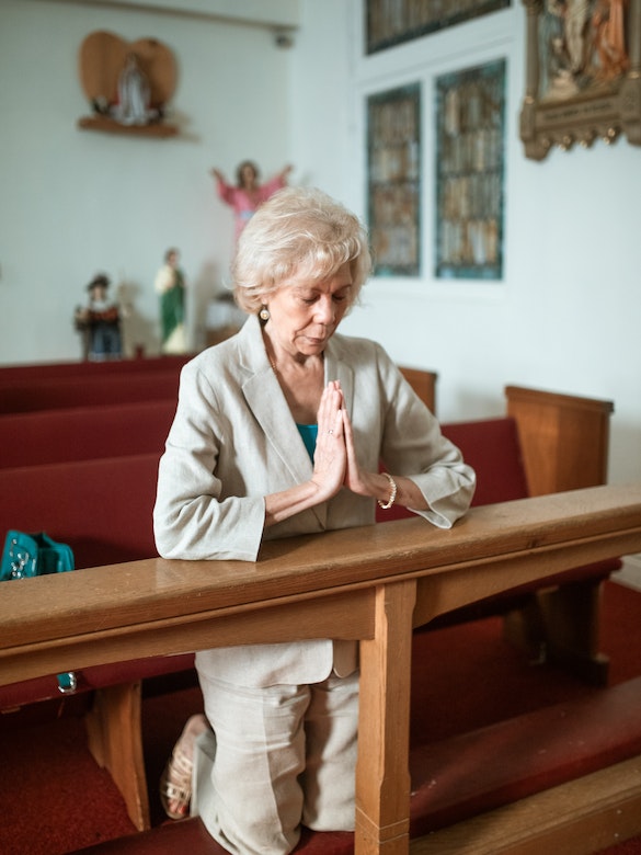an elder woman kneels at an altar alone and prayer to the Lord