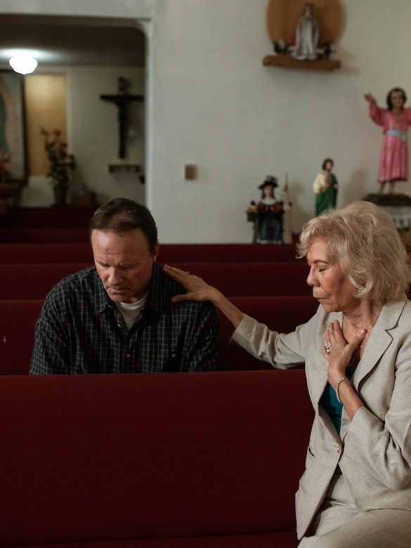 a woman prays for a man in a pew at church