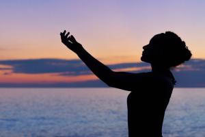 silhouette of woman with arms raised up as if in worship