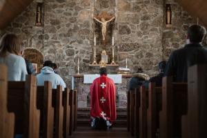 Priest kneeling at altar with back towards congregation