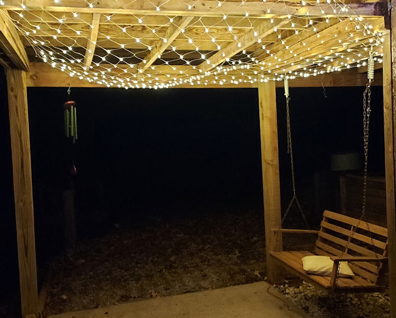 Picture of a porch at night being lit by a net of white lights