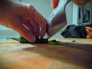 Close up of a cefs hand and steel knife blade cutting vegetables on a wooden block