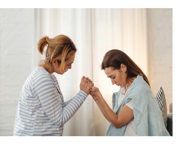 two women holding hands praying