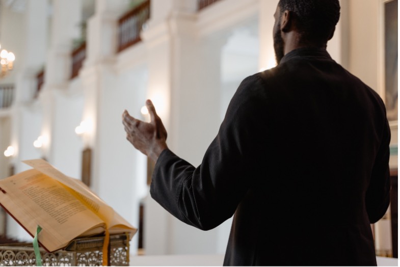 Black man at podium with open bible hand spread