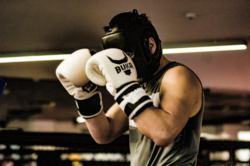 Boxer with black helmet, blocking face with white gloves